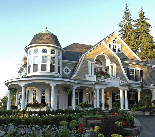 House plan exterior of a two-story home with a prominent round tower, wraparound porch, and gambrel rooflines.