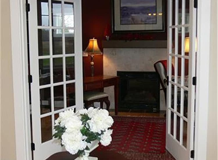 Interior view of a room with french doors, fireplace, desk, and a vase of white flowers.