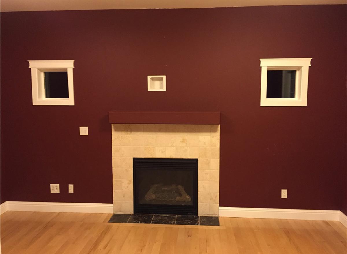Living room with fireplace, two square windows, and wood flooring.