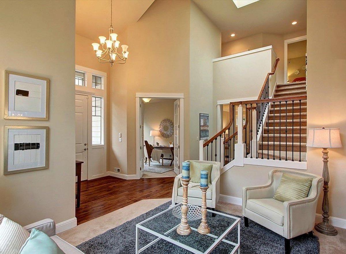 Interior view of a house foyer with a vaulted ceiling, chandelier, open staircase with wood banister, and double doors leading to a home office.