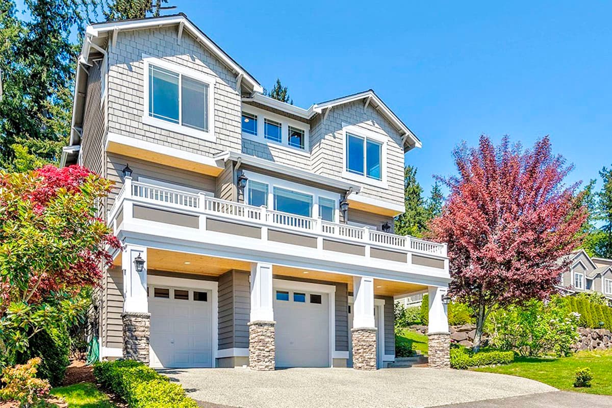 House plan exterior: Three-story home with shingle siding, wrap-around balcony, and three-car garage.