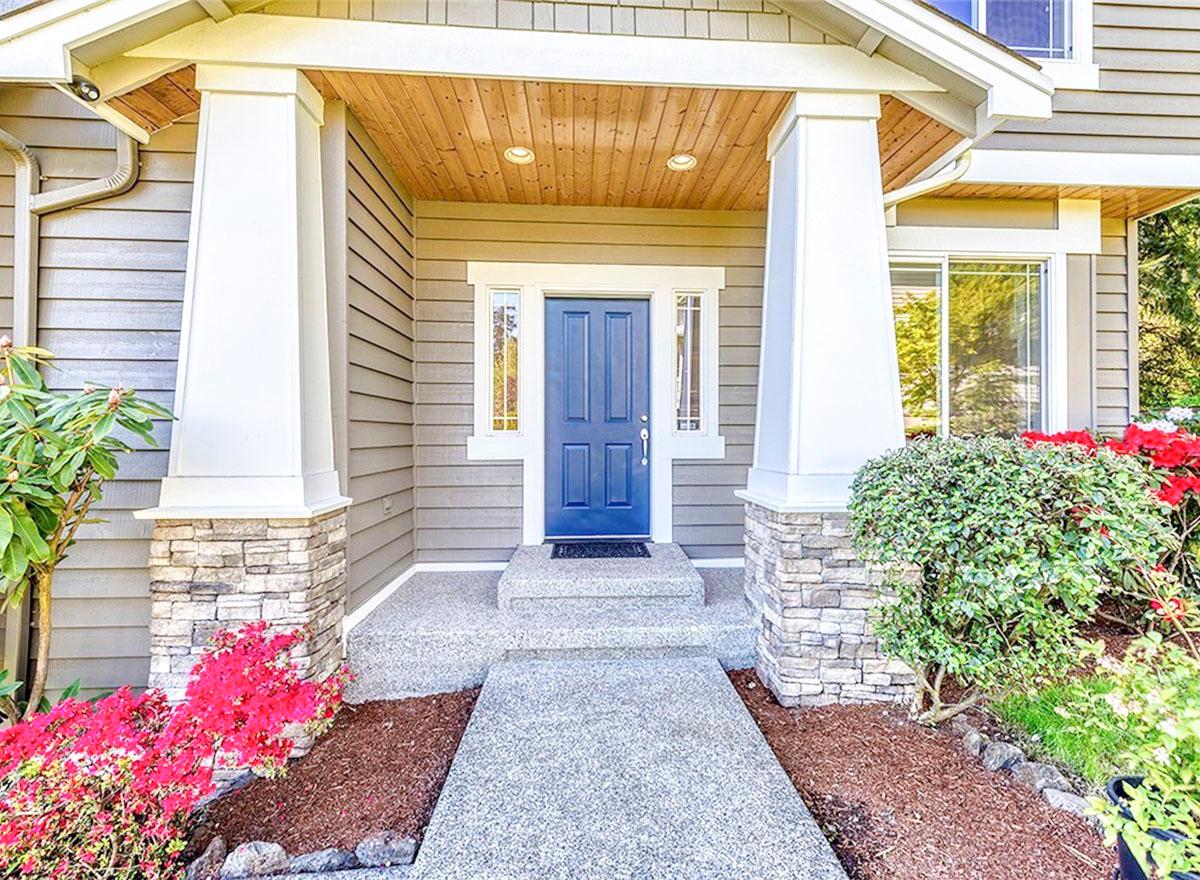 House plan exterior featuring a covered front porch with stone-clad columns, a blue paneled door, and horizontal siding.