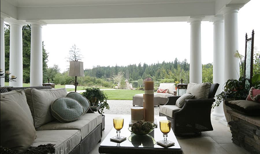 House plan exterior featuring a wide covered porch supported by Doric columns with outdoor seating and a natural landscape view.
