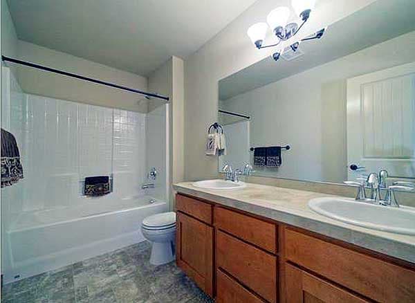 Bathroom with tub-shower combo, toilet, and double vanity with wood cabinets and large mirror.
