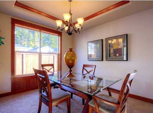 Dining room with glass-top table, wooden chairs, large window with wood trim, and coffered ceiling.