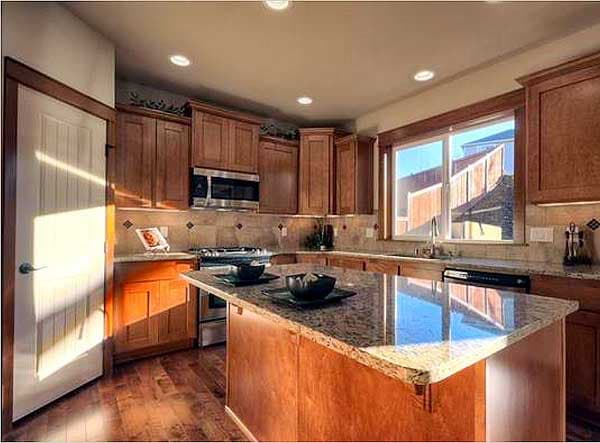 Kitchen with wood cabinetry, granite countertops, island with seating, stainless steel appliances, and large window.