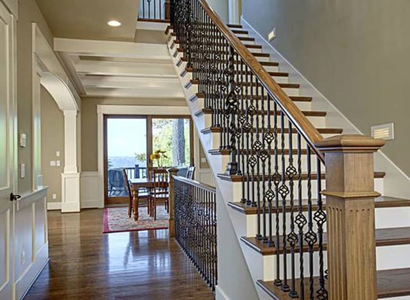 Interior view of a house with coffered ceiling, wood staircase with ornate metal balusters, and dining area with sliding glass doors.