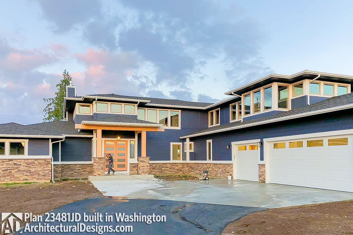 Modern house plan exterior with dark blue siding, stone accents, covered entry with wood posts, and a triple-bay garage.