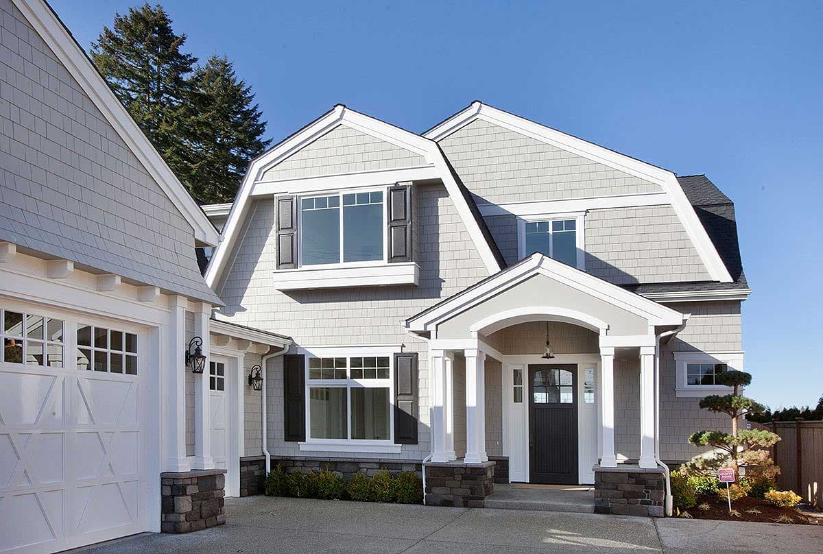House plan exterior: Two-story home with gambrel roof, front porch with arched entrance, attached garage, and shingle siding.