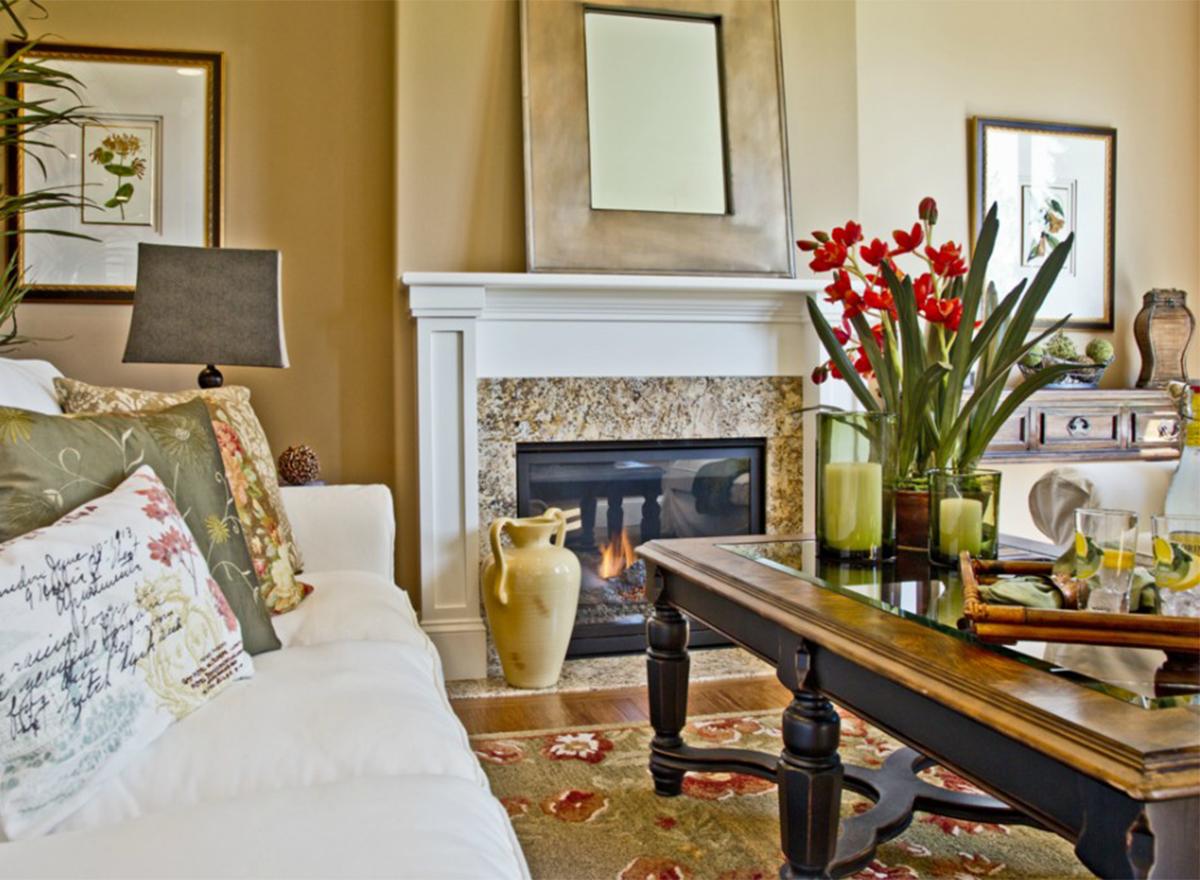 Living room interior featuring a white sofa, fireplace with granite surround, and coffee table. Includes decorative pillows and floral arrangements.