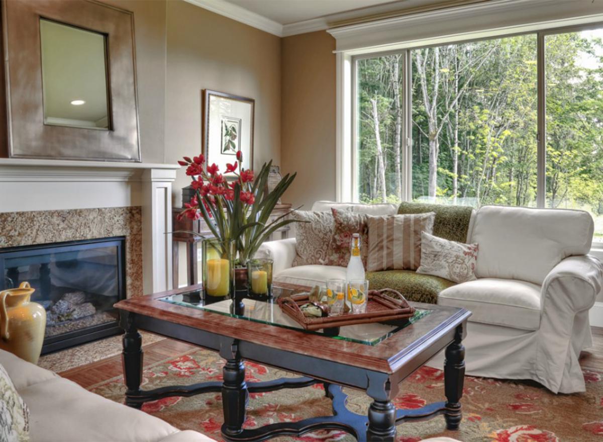 Living room interior with fireplace, large window overlooking trees, and plush seating.