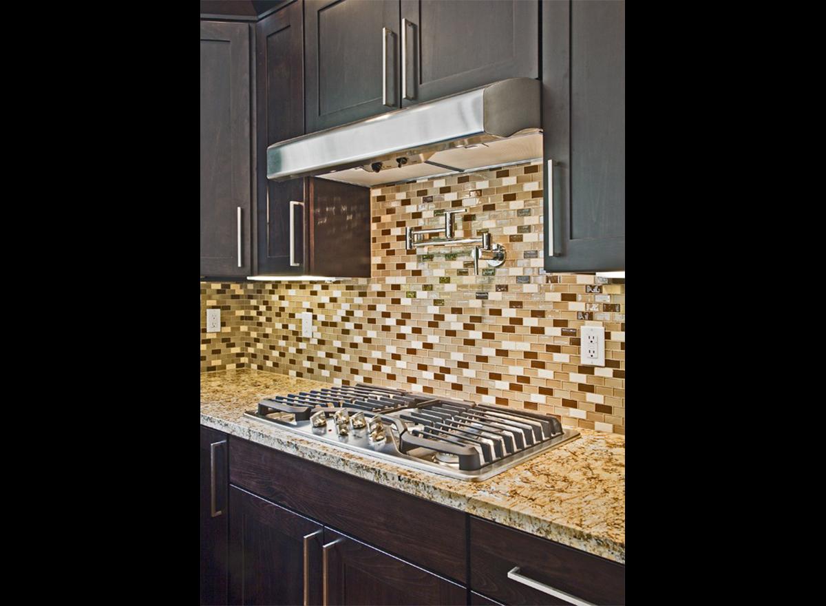 Kitchen gas range with pot filler faucet and mosaic tile backsplash set against dark wood cabinets.