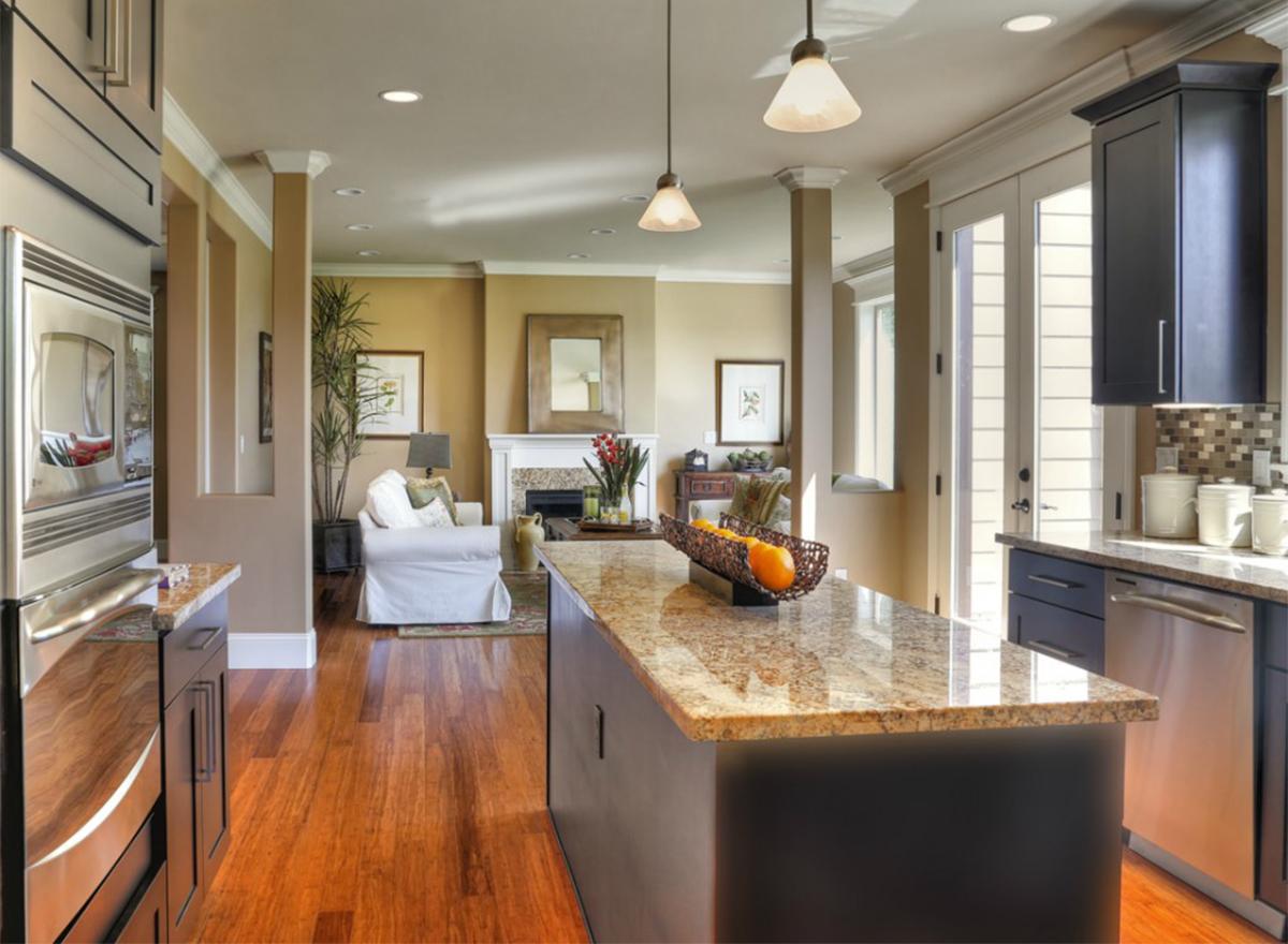 Open concept kitchen and great room with fireplace, island, dark cabinets, and french doors.