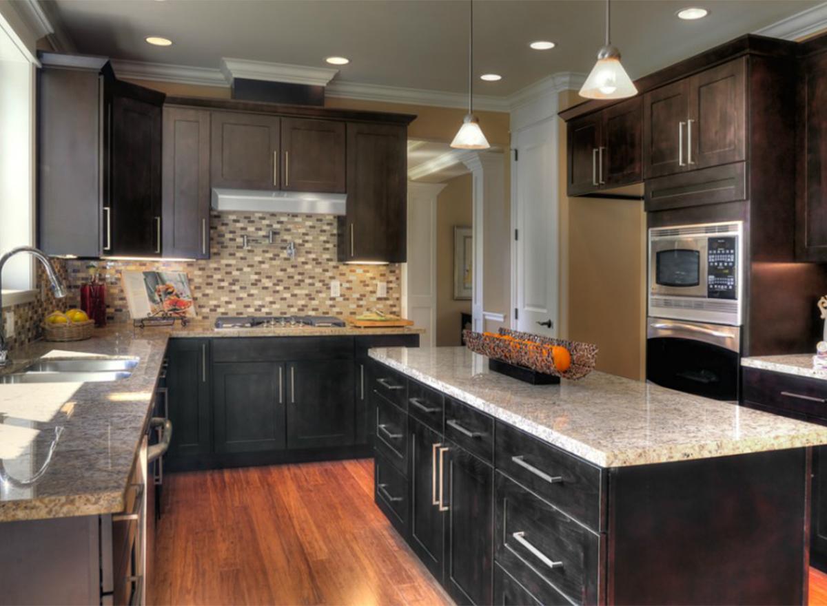 Kitchen with dark wood cabinetry, granite countertops, stainless steel appliances including a microwave and range hood, and a central island.