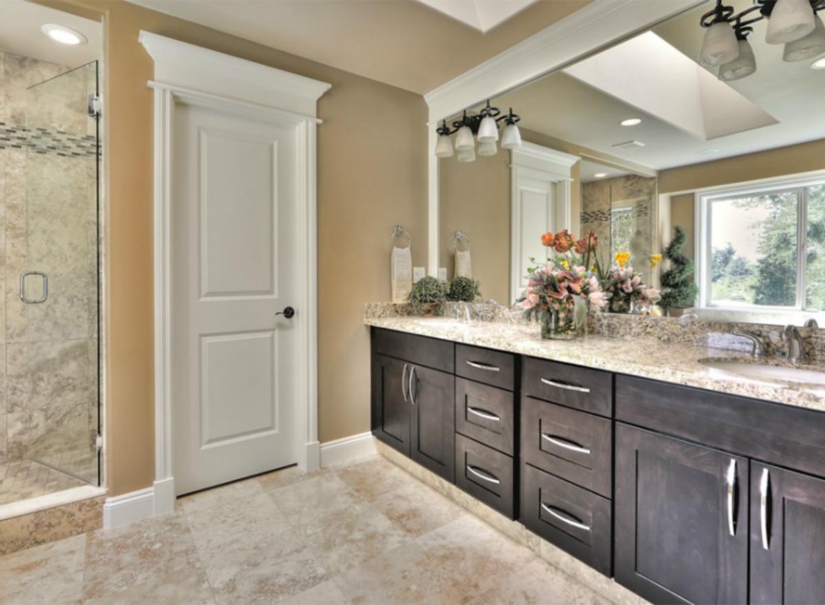 Bathroom vanity with dark wood cabinets, granite countertop, double sinks, and a glass-enclosed shower.