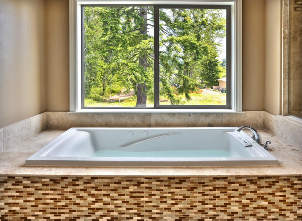 Bathroom interior featuring a built-in soaking tub with mosaic tile surround and a large window overlooking trees.