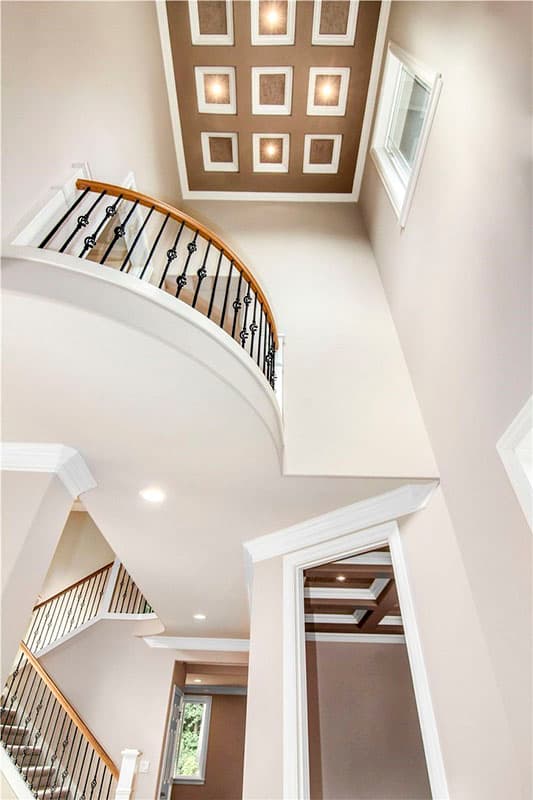 Interior view of a grand entryway with a curved staircase, coffered ceiling, and wrought iron railings.