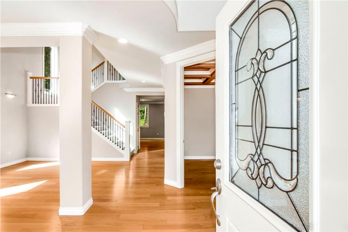Interior view of a foyer with hardwood floors, a staircase with black spindles, and an open doorway revealing a wood-paneled ceiling.