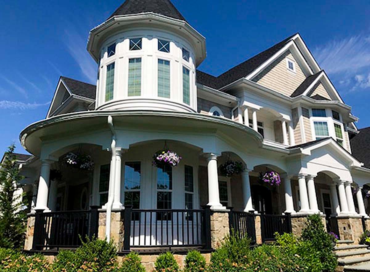 House plan exterior with a prominent round tower, wraparound porch with columns, gables, and dormers.