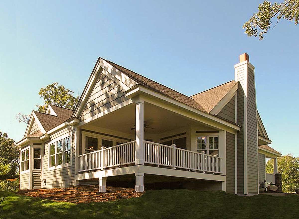 House plan exterior featuring a covered porch with white railings, gables with shaker siding, and a prominent stone-clad chimney.