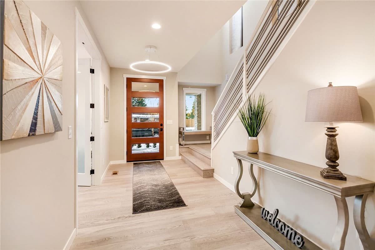 Interior view of a modern entryway with a wood door, circular pendant light, and open staircase with metal railings.