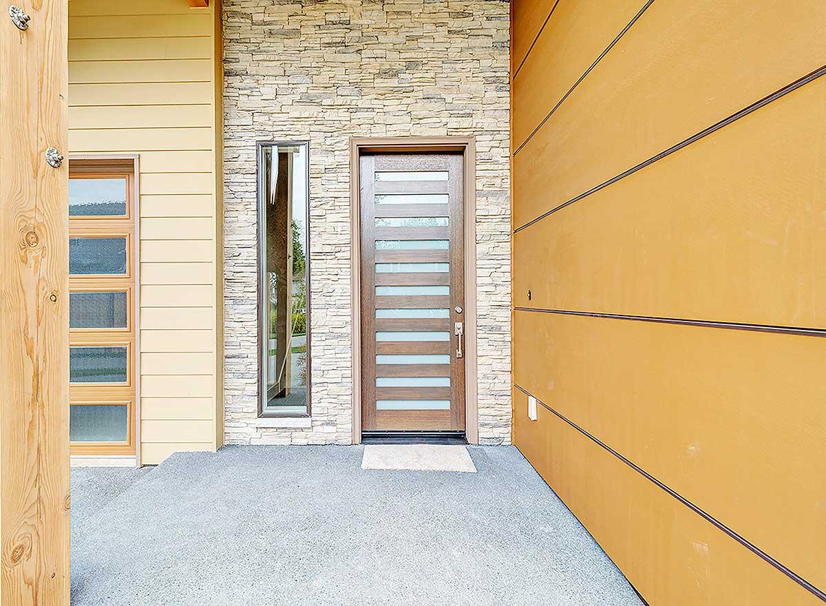 Modern house exterior featuring a wood door with glass panes, stacked stone accent, and horizontal siding.