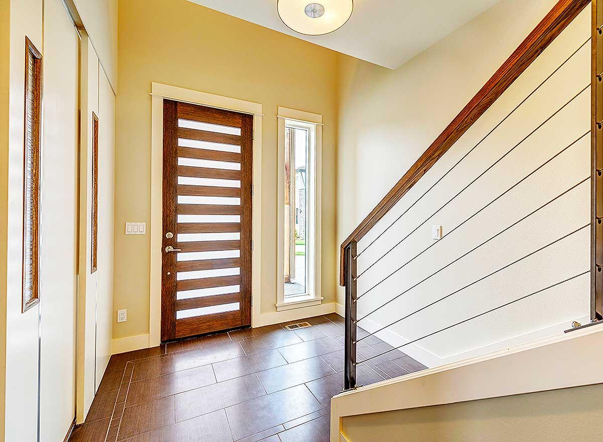 Modern entryway with horizontal wood door, narrow vertical window, and cable railing staircase.