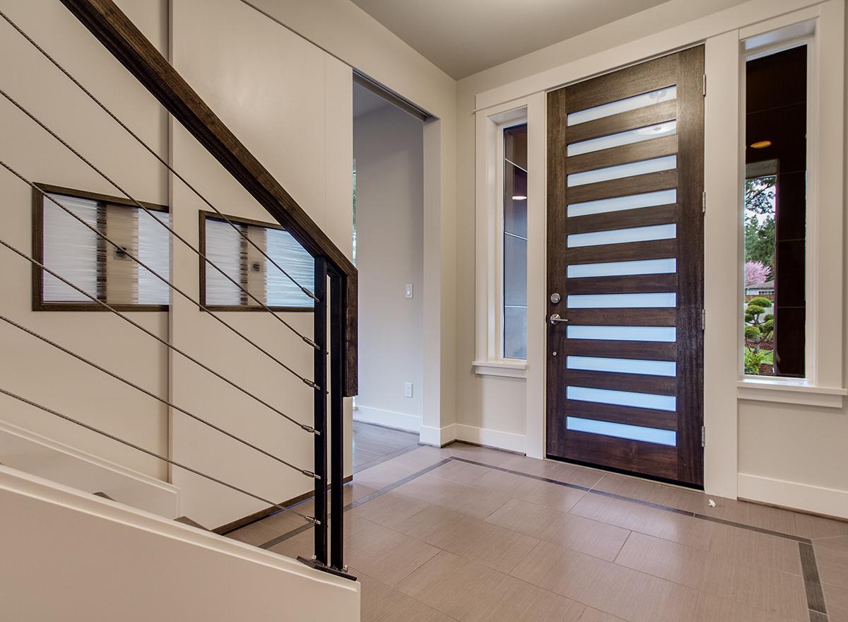 Modern entryway with wood door featuring horizontal glass panes and cable railing staircase.