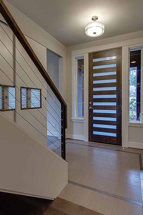 Interior view of a foyer with a modern wood door featuring horizontal glass panels and a cable railing staircase.