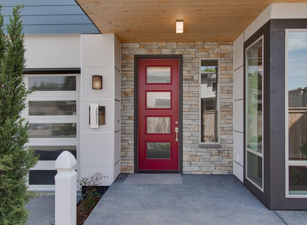 Modern house plan exterior with red door, stone facade, horizontal garage door, and wood ceiling.