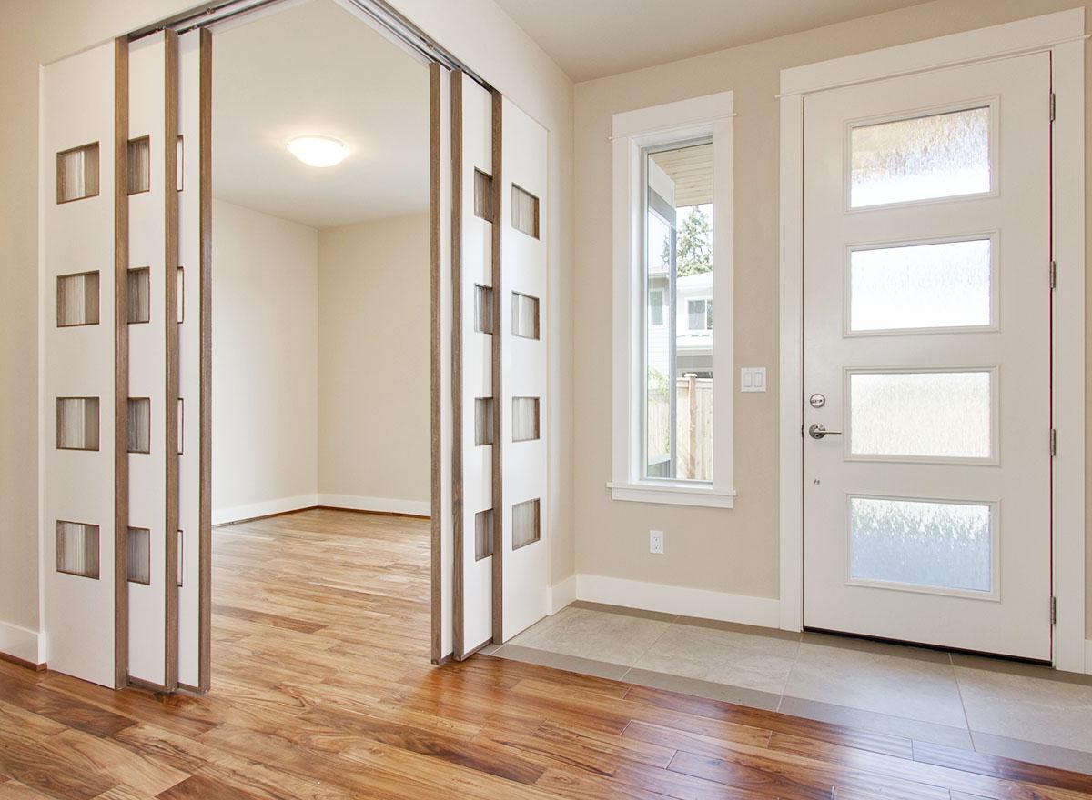 Interior view showing folding doors with square glass panels, a modern entry door with three glass panes, and a tall window.