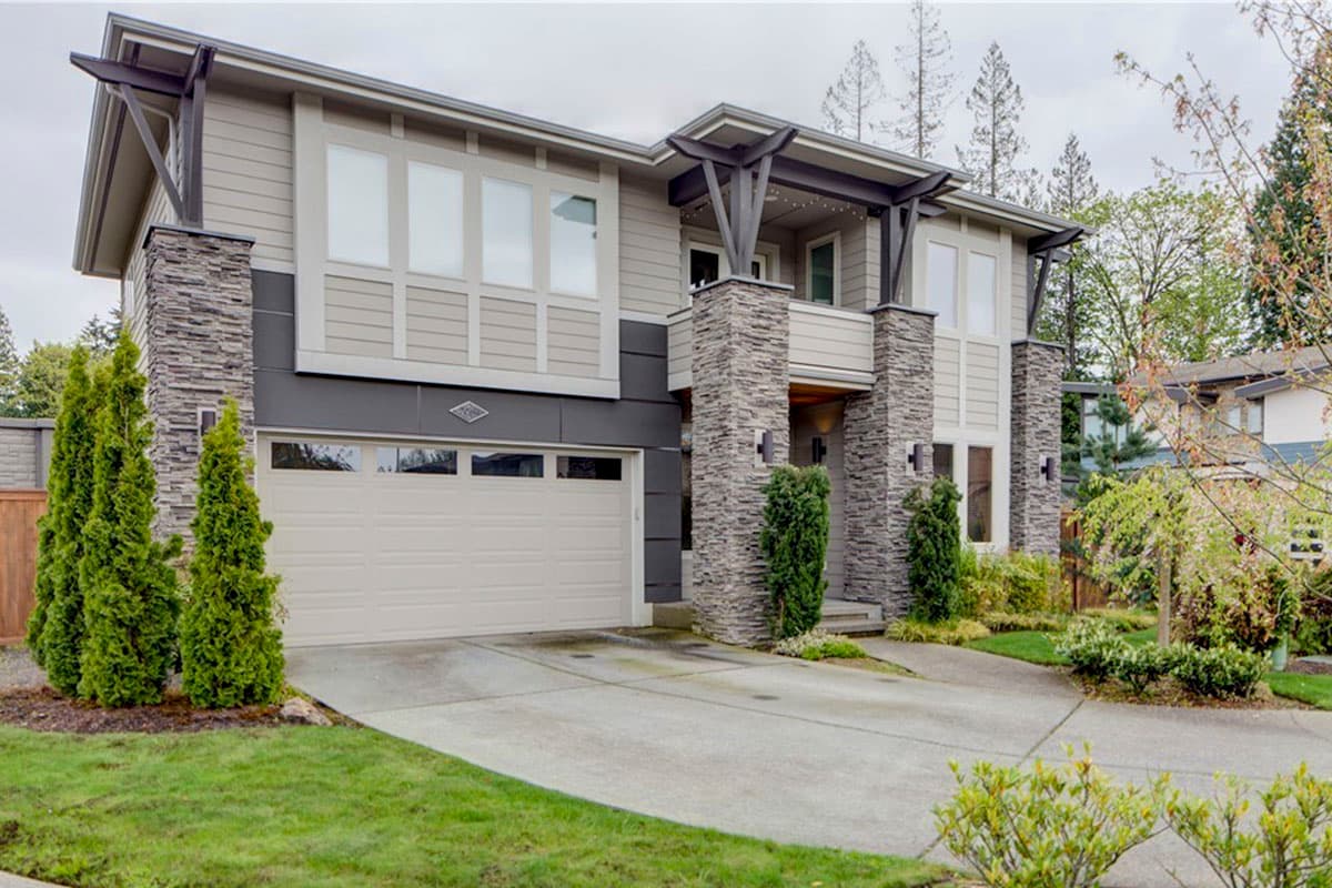 Two-story modern house plan exterior with stone accents, horizontal siding, a covered balcony, and a two-car garage.