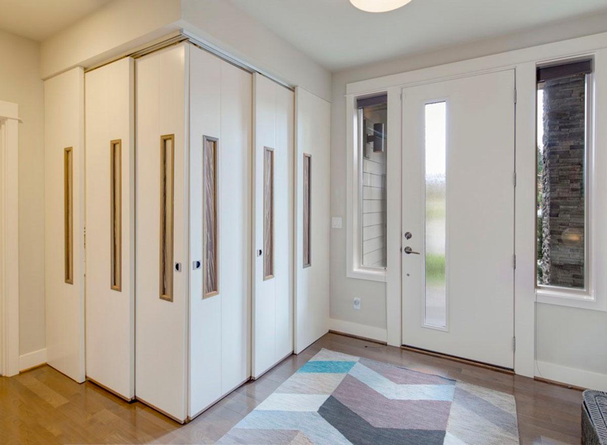 Interior view of entryway with wall of white bi-fold doors with wood insets and a frosted glass front door with sidelights.
