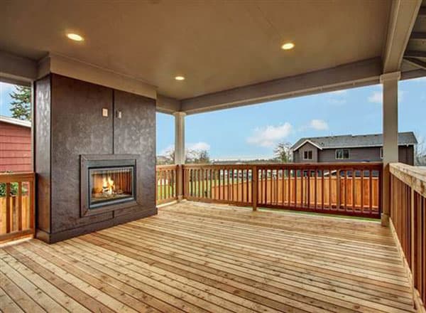 Covered outdoor living space with a wood deck, built-in fireplace, and wooden railings.