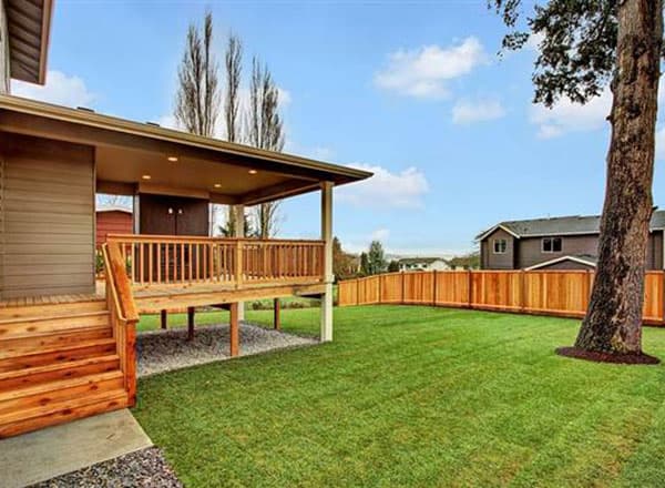 House plan exterior view of a covered deck with wooden railings and stairs, adjacent to a fenced backyard.