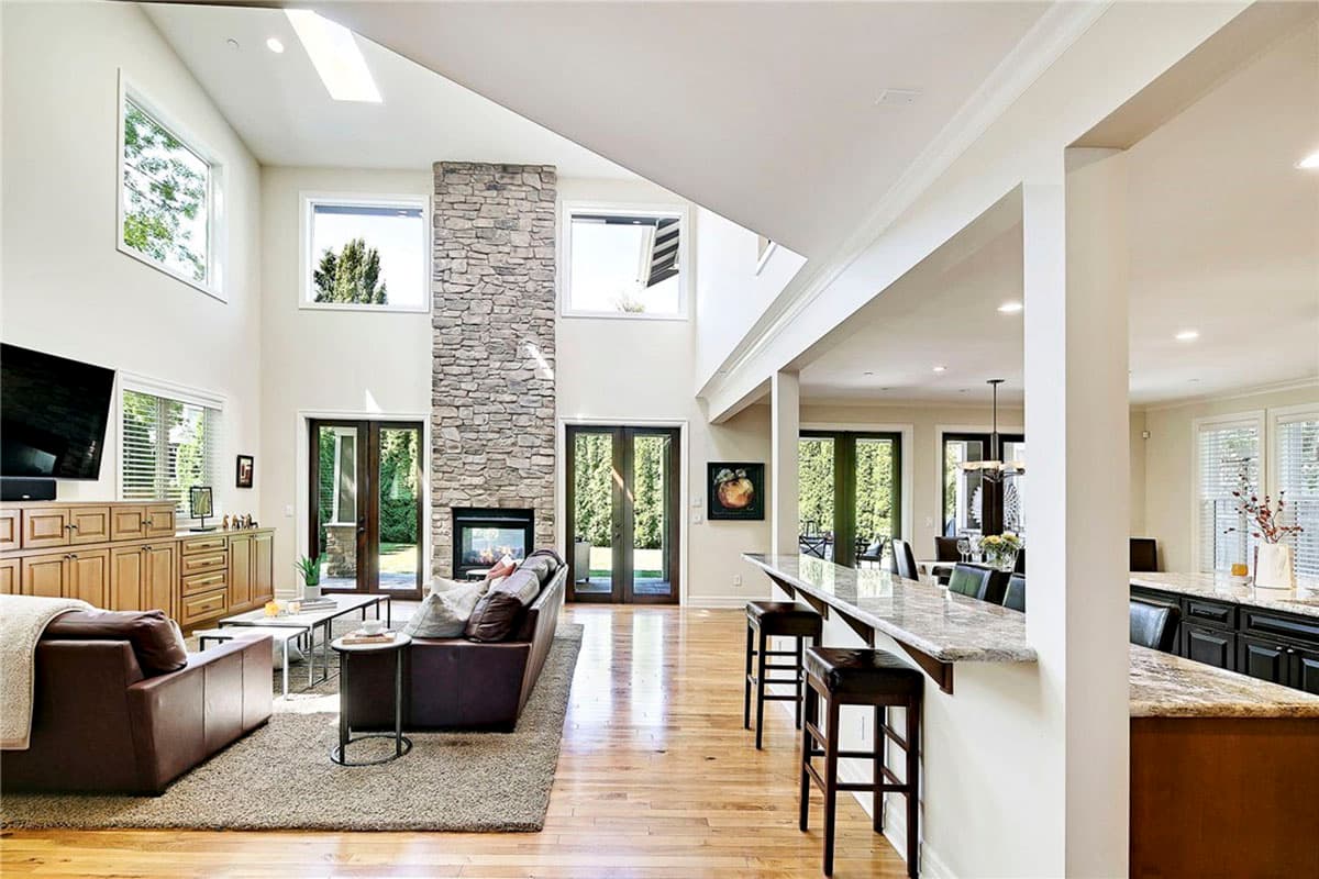 Interior view of open-concept living area with vaulted ceiling, stone fireplace, and kitchen island with bar seating.