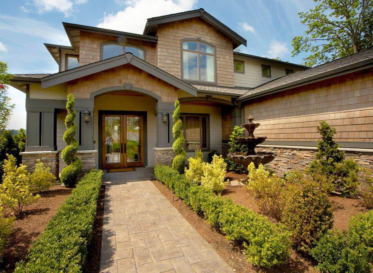 House plan exterior with arched entry, double doors, wood shake siding, stone accents, and layered rooflines.