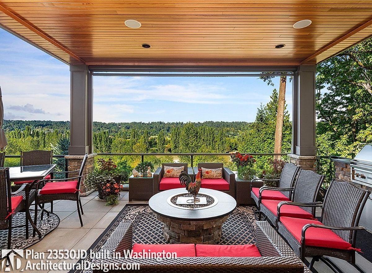 Covered deck with seating, fire pit, dining table, and grill overlooking a wooded landscape.
