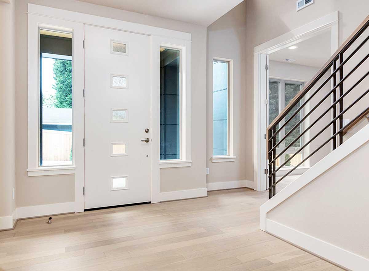 Modern house plan entryway with white door, sidelight windows, narrow vertical windows, and a contemporary staircase with metal railing.