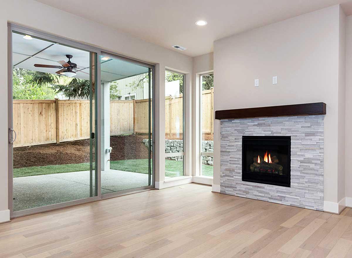 Interior view of a living area with a stone fireplace, dark wood mantel, and large sliding glass doors opening to a patio.