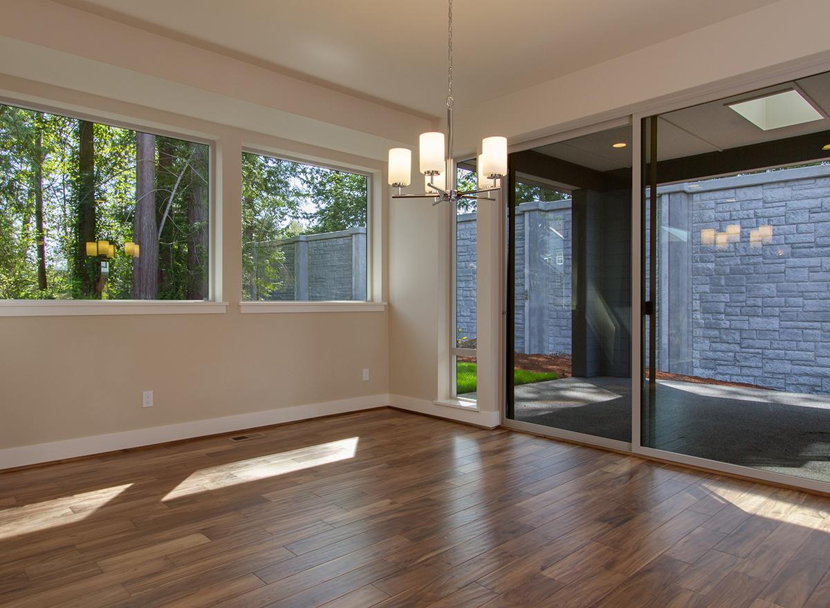 Interior view of a dining room with wide windows and sliding glass doors opening to an outdoor patio with stone walls.