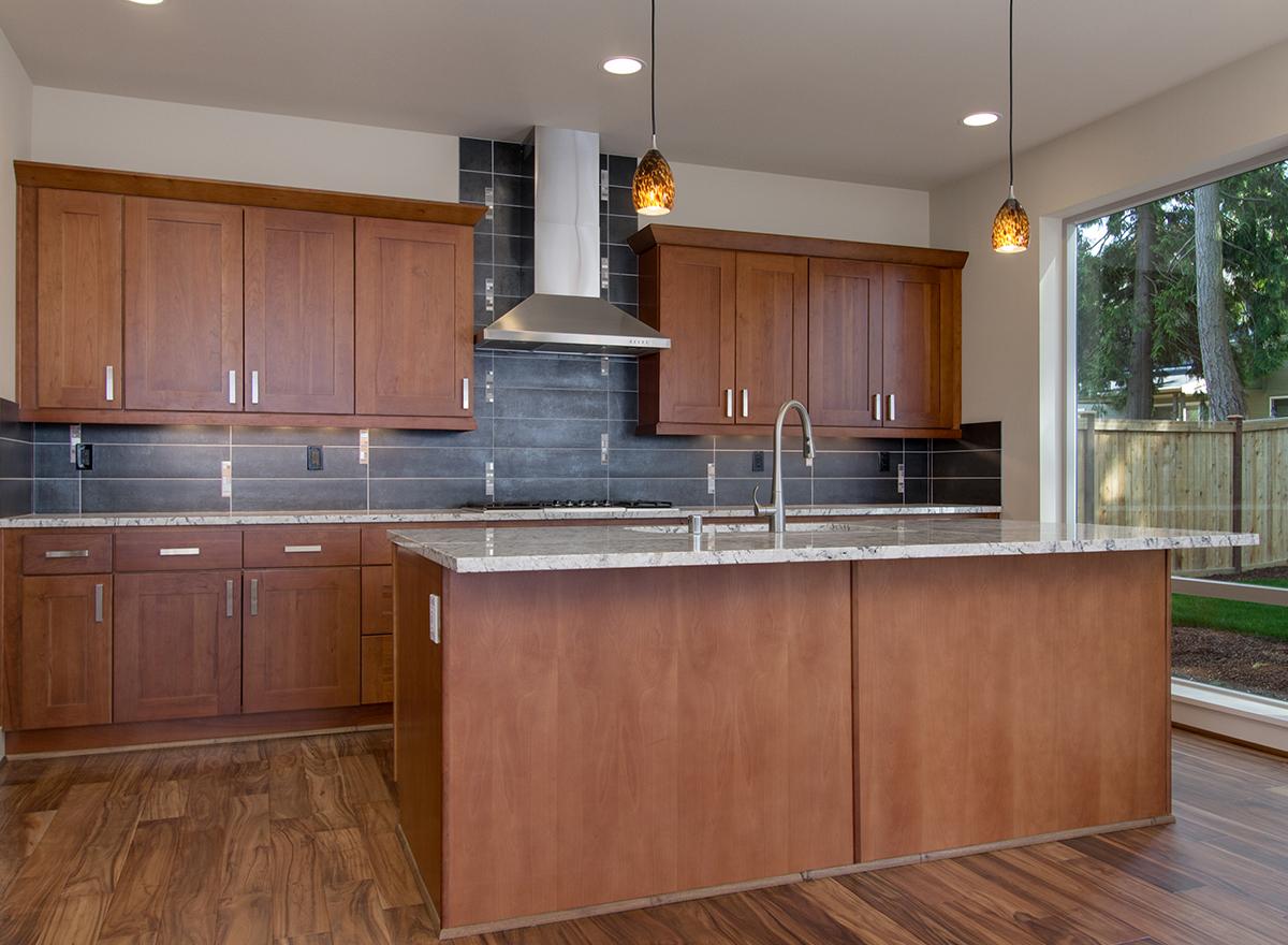 Kitchen interior with cherry wood cabinets, granite countertops, island sink, stainless steel range hood, and large window.