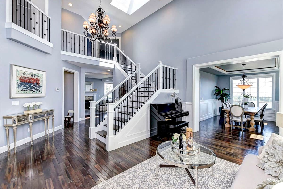 Interior view of grand foyer with two-story open-concept design, open staircase with black balusters, and adjacent dining room.