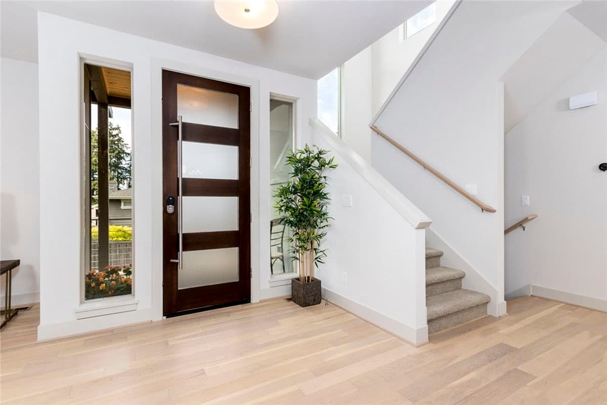 Modern entryway with frosted glass panel door, vertical windows, and carpeted staircase with wood handrail.