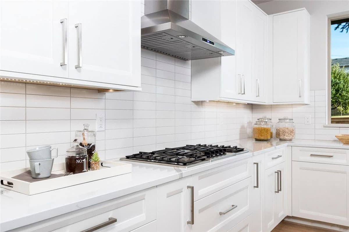 Kitchen with white Shaker cabinets, white subway tile backsplash, stainless steel gas range, and island.