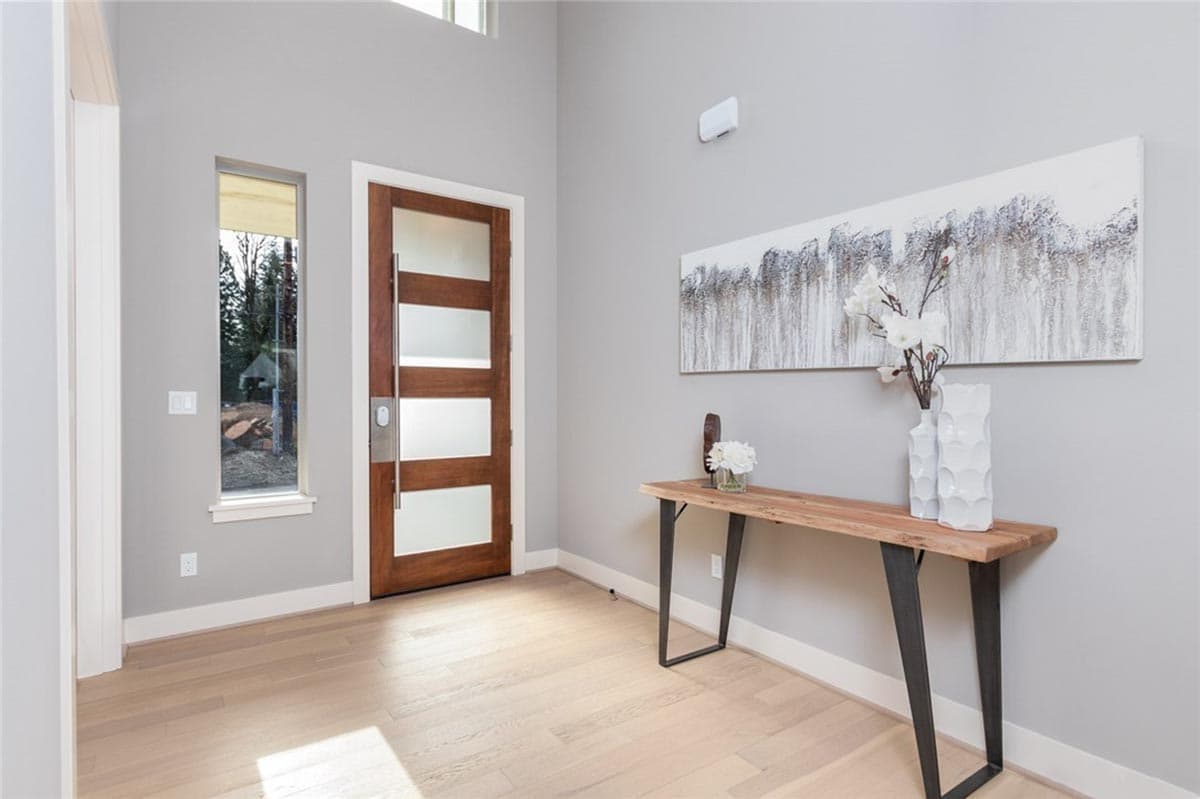 Modern entryway with tall wooden door with frosted glass panels, narrow vertical window, and console table.