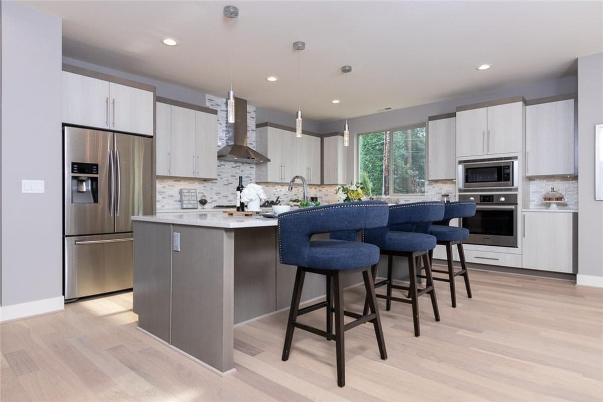 Modern kitchen with island, stainless steel appliances, dual-tone cabinets, and pendant lighting.