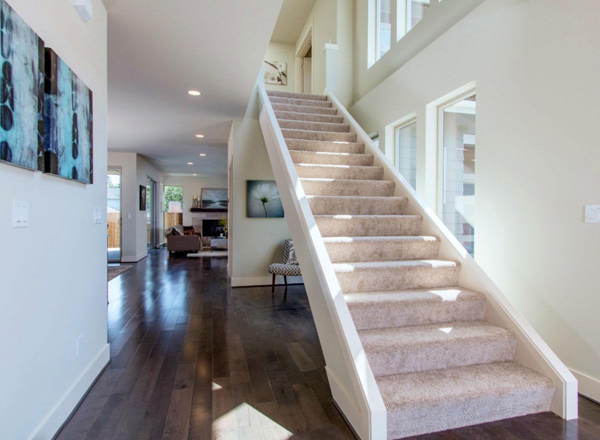 Interior view of home entryway with carpeted staircase, dark wood floors, and view into living area with fireplace.