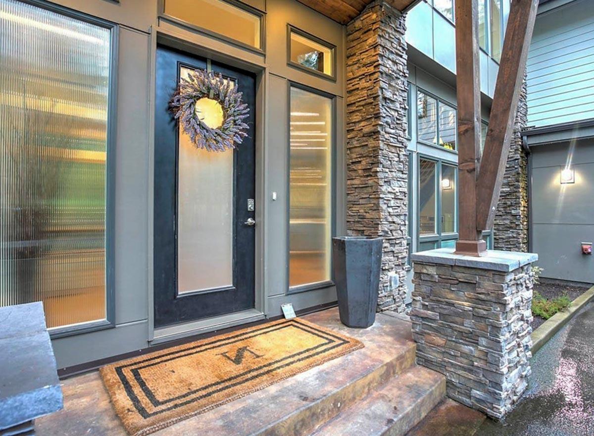 Exterior house plan: Modern style with stone facade, covered entry with dark door, sidelight windows, and prominent wood beams.