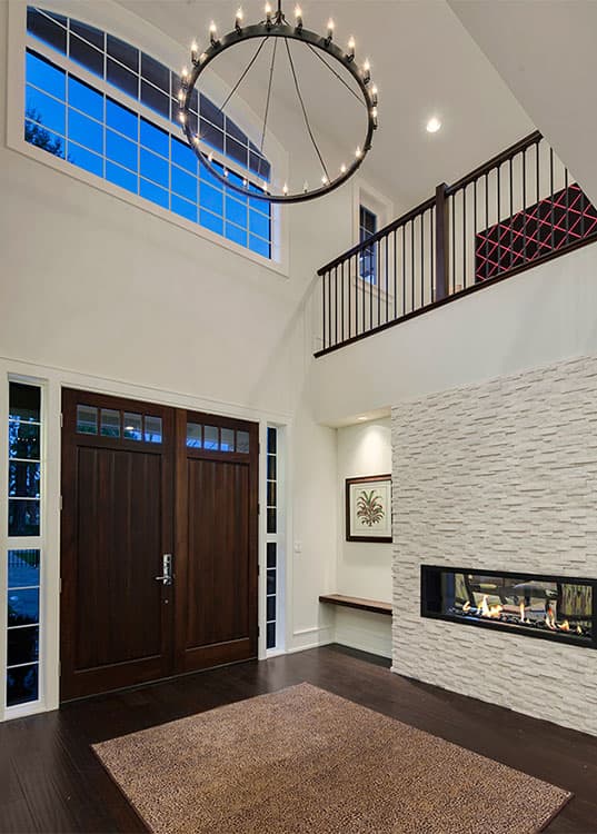 Interior view: Double front doors open to a foyer with a two-story ceiling, large windows, and a linear gas fireplace.